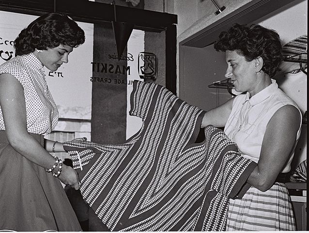 רות דיין (מימין) ומלכת היופי שרה טל, אוחזות בחולצה בחנות "משכית", 1956